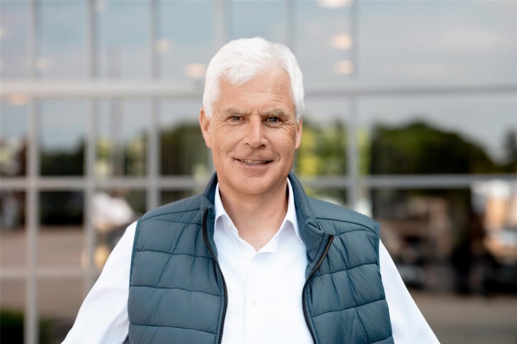 Thomas Heinzel blickt in die Kamera. Er trägt ein weißes Hemd unter einer grünen Weste und lächelt leicht. Thomas Heinzel blickt in die Kamera. Er trägt ein weißes Hemd unter einer grünen Weste und lächelt leicht.