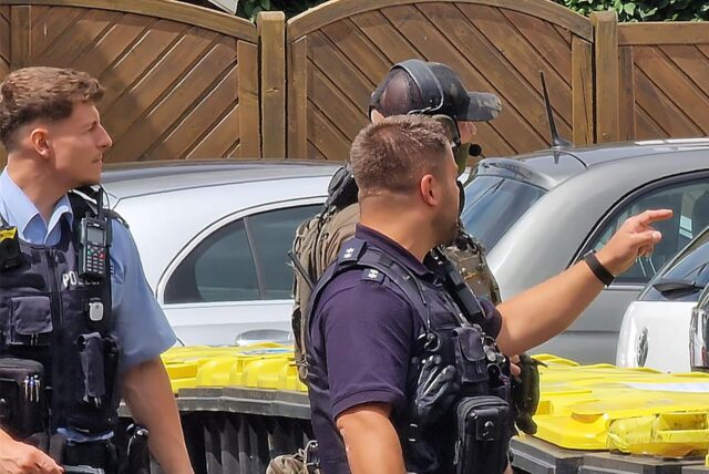 Vor einem weißen Mehrfamilienhaus führen Polizisten eine Bewohnerin ab, die sich der Zwangsräumung widersetzt hatte.