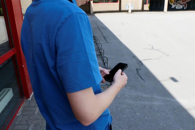 Ein Junge nutzt sein Smartphone auf dem Schulhof.