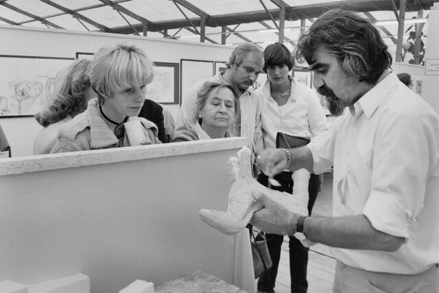 Ein Schwarz-Weiß-Bild. Prof. Lothar Kampmann fertigt beim 5. Bergkamener Bilder Basar (BBB) 1980 eine Skulptur an, drei Frauen und zwei Männer schauen zu.