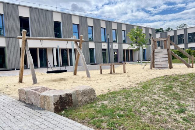 Auf dem Außengelände einer neuen Grundschule und einer neuen Kita in Unna ist ein Spielplatz mit Schaukel und Klettergerüst