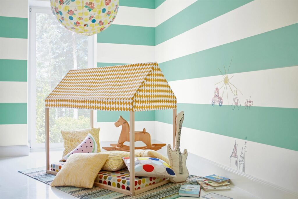 Ein Spielhaus steht in einem Kinderzimmer vor einer Tapete mit horizontalem Streifenmuster Ein Spielhaus steht in einem Kinderzimmer vor einer Tapete mit horizontalem Streifenmuster