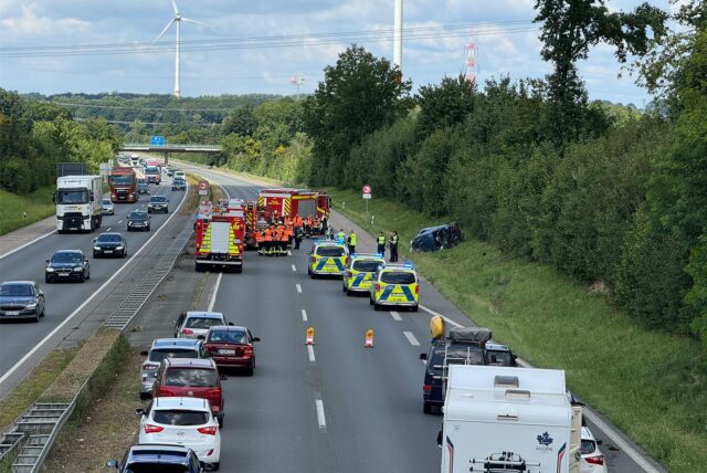 Mehrere Einsatzfahrzeuge stehen auf der A1 Richtung Bremen nahe der Anschlussstelle Hamm/Bergkamen/Werne. Die Autobahn ist gesperrt, es gibt Stau. Rechts auf der Wiese ein Wagen, der sich überschlagen hat.