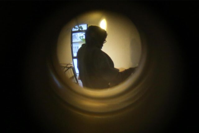 Ein Symbolfoto zum Thema Einbrecher zeigt den Blick durch einen Türspion. Vor der Wohnung teht eine dunkle Gestalt.