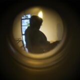 Ein Symbolfoto zum Thema Einbrecher zeigt den Blick durch einen Türspion. Vor der Wohnung teht eine dunkle Gestalt.