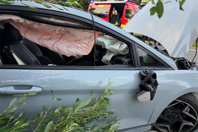 Ein stark beschädigtes weißes Auto im Straßengraben, erkennbar haben die Airbags gezündet.