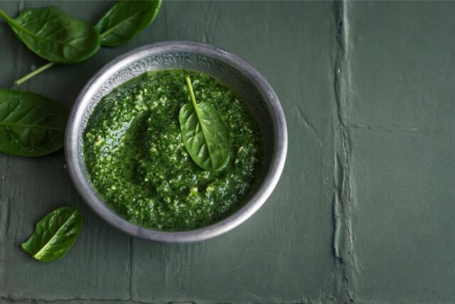 Pesto Verde in einer Schale – daneben liegen Basilikum-Blätter.