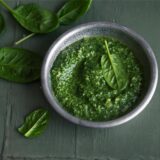 Pesto Verde in einer Schale – daneben liegen Basilikum-Blätter.