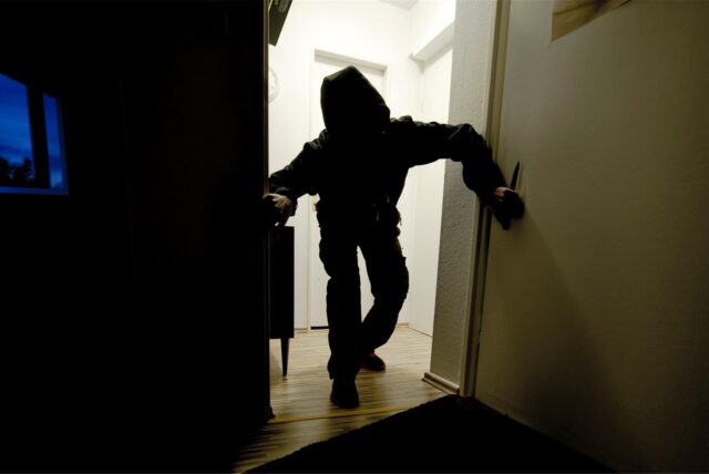 Ein Mann mit heruntergezogener Kapuze bricht in ein Haus ein. (Symbolfoto)