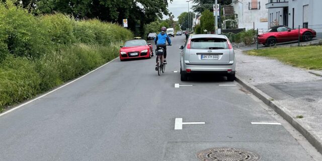Ein Radfahrer fährt auf dem Afferder Weg zwischen einem stehenden und einem fahren Auto hindurch.