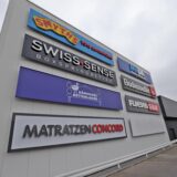 Fassadenansicht eines Gewerbe-Komplexes mit Logos mehrerer Einzelhandelsgeschäfte in Kamen am Zollpost, darunter Smyths Toys, Swiss Sense, Matratzen Concord und weitere.