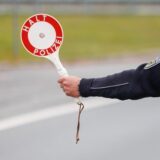 Polizeibeamter in Uniform hält Kelle mit „Halt Polizei“-Schild bei Verkehrskontrolle auf einer Straße.