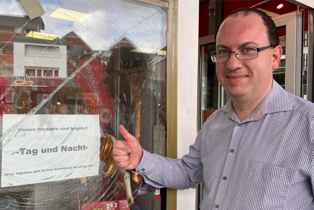 Mitarbeiter Marco Weidlich steht vor der zersplitterten Scheibe seines Vodafone-Ladens in Kamen. Er zeigt den Daumen nach oben und lächelt in die Kamera.