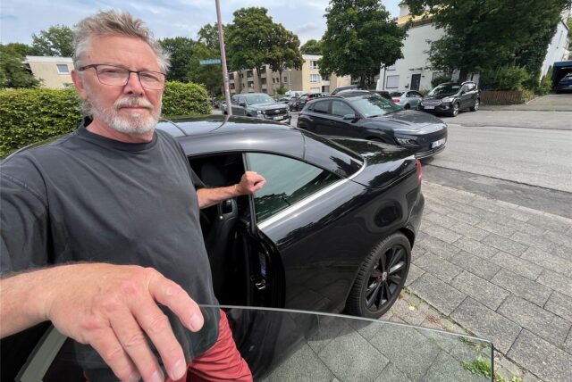 Andreas Blees aus Unna steht an der offenen Tür seines Autos auf seinem Garagen-Vorplatz an der Eichenstraße. Dahinter ragt ein Fahrzeug in die Ausfahrt hinein.