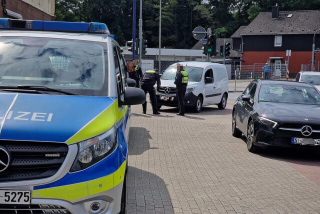 Bei einer Kontrollaktion in Unna steht ein Polizeiauto an einer Straße, dahinter stehen Polizisten vor einem weißen Auto