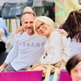 Ein Mann und eine Frau sitzen Arm in Arm beim Feierabendmarkt auf dem Marktplatz in Schwerte. Sie sind von weiteren Menschen umgeben.