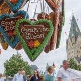 Lebkuchenherzen mit der Aufschrift „Gruß von Libori“ hängen an einem Stand der Libori-Kirmes in Paderborn. Im Hintergrund sind Besucher und der Dom zu sehen.