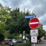 Verkehrsschilder am Koepeplatz in Kamen: Einfahrt verboten, Fahrrad frei, Richtungsweisung für Radfahrer, geparkte Autos und Bäume im Hintergrund. Hier wird es bald zu Baumschnittarbeiten der Stadt kommen.