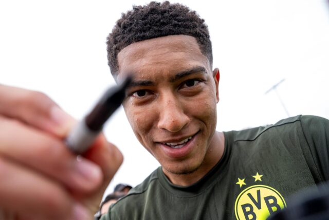 Jobe Bellingham hält einen Stift in der Hand und in eine Kamera-Linse.