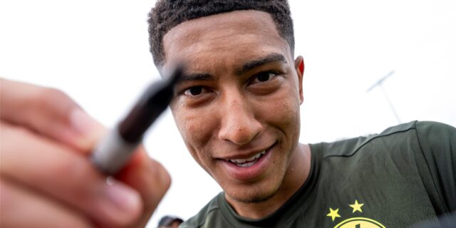 Jobe Bellingham hält einen Stift in der Hand und in eine Kamera-Linse.
