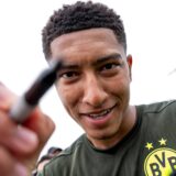 Jobe Bellingham hält einen Stift in der Hand und in eine Kamera-Linse.