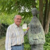 Wolfgang Miehle steht neben einer Bronzefigur in seinem Garten.