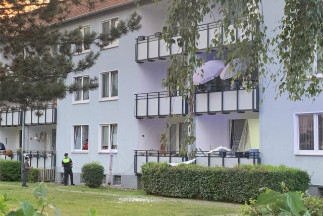 Ein Polizist steht vor dem Mehrfamilienhaus an der Distelfinkstraße in Bergkamen und spricht mit Bewohnern.