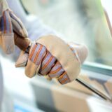 Mit Handschuhen geschützt hebeln zwei Hände mit einem Stemmeisen ein Fenster auf.