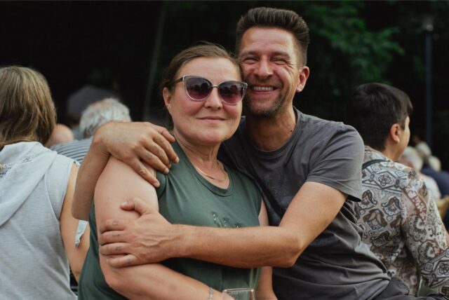 Besuchende des Sommer-Pop-Konzerts 2025 im Sesekepark in Kamen. Ein Mann umarmt eine Frau. Beide schauen in die Kamera, im Hintergrund sind viele andere Menschen.
