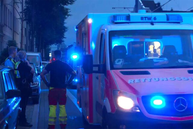 Polizisten stehen bei einem Einsatz vor einem Rettungswagen mit Blaulicht.