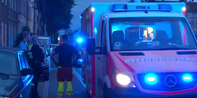 Polizisten stehen bei einem Einsatz vor einem Rettungswagen mit Blaulicht.