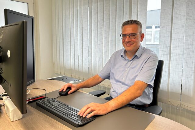 Dr. Adam Dimitros Exarchos, Facharzt für Kinder- und Jugendmedizin sowie Kinderkardiologe, sitzt in seiner Praxis am Willy-Brandt-Platz in Kamen an seinem PC, er lächelt.