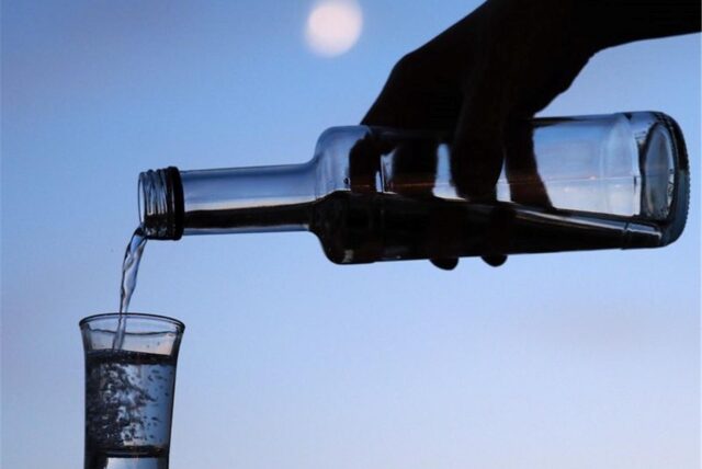 Zu vorgerückter Stunde wird Wodka aus einer Flasche in ein Schnapsglas geschüttet. Im Hintergrund ist der Mond zu sehen.
