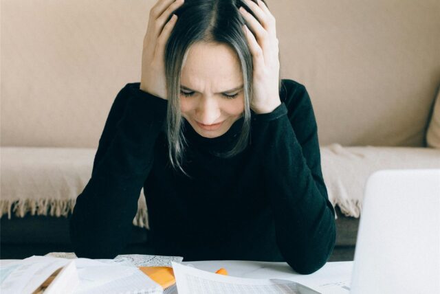 Eine Frau sitzt verzweifelt vor Rechnungen. Mieter können Mietpreise, die die Vergleichsmiete deutlich überschreiten, bei der Stadt melden. (Symbolbild)