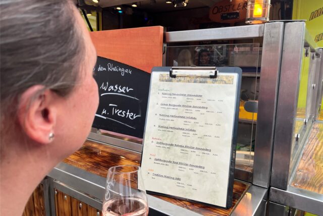 Eine Frau studiert die Weinkarte am Stand des Winzers aus dem Rheingau.