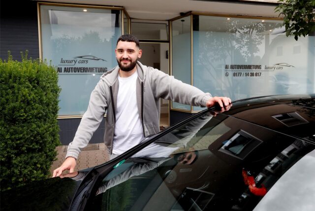 Vor dem Ladenlokal in Rünthe mit der Aufschrift „AI Autovermietung“ steht Inhaber Armend Ibishi mit einem Auto.