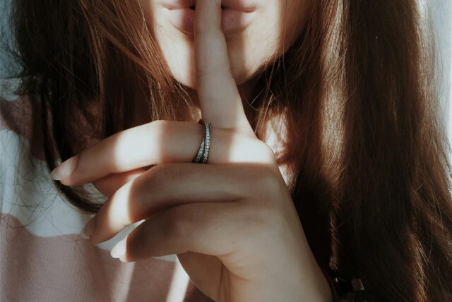 Eine Frau hält einen Zeigefinger auf ihren Mund und deutet an zu schweigen.