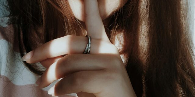 Eine Frau hält einen Zeigefinger auf ihren Mund und deutet an zu schweigen.