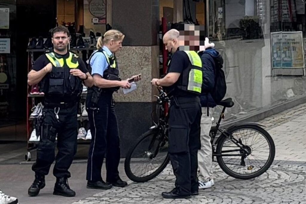 Drei Polizeibeamte stehen an einer Ecke des Unnaer Marktplatzes und sprechen mit einem Mann, der dort mit dem Fahrrad unterwegs war. Im Hintergrund ist ein Schuhgeschäft zu erkennen.