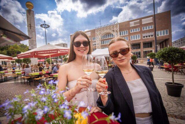 Zwei Besucherinnen des Weinsommers 2025 auf dem Friedensplatz in Dortmund halten ihr Weinglas in die Kamera.